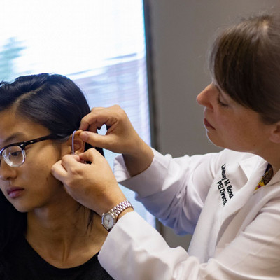 audiologist fitting hearing aid on patient