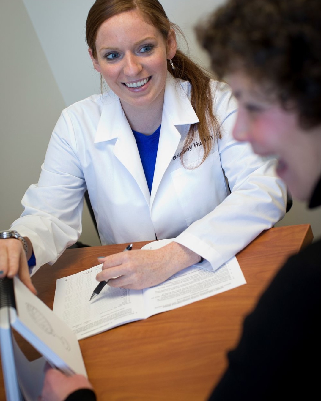 woman holding a pen and paper talking to another woman