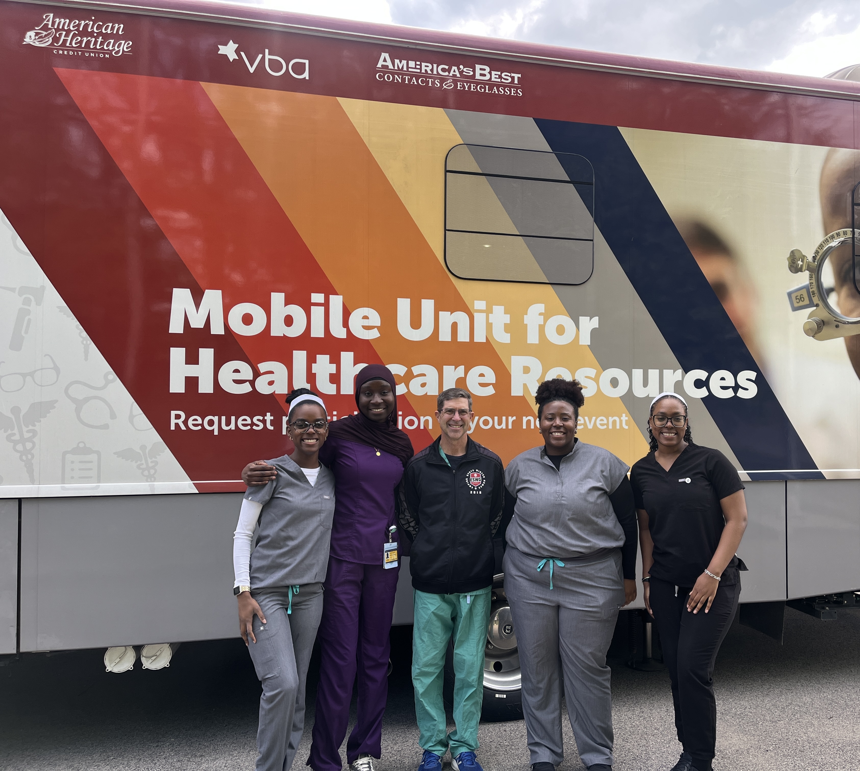 group photo of optometry students and doctor in front of bus